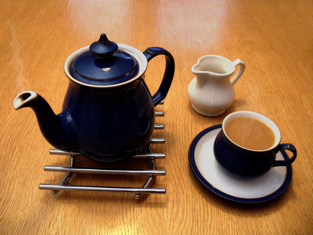 Tea pot next to a cup of tea and a small milk jug